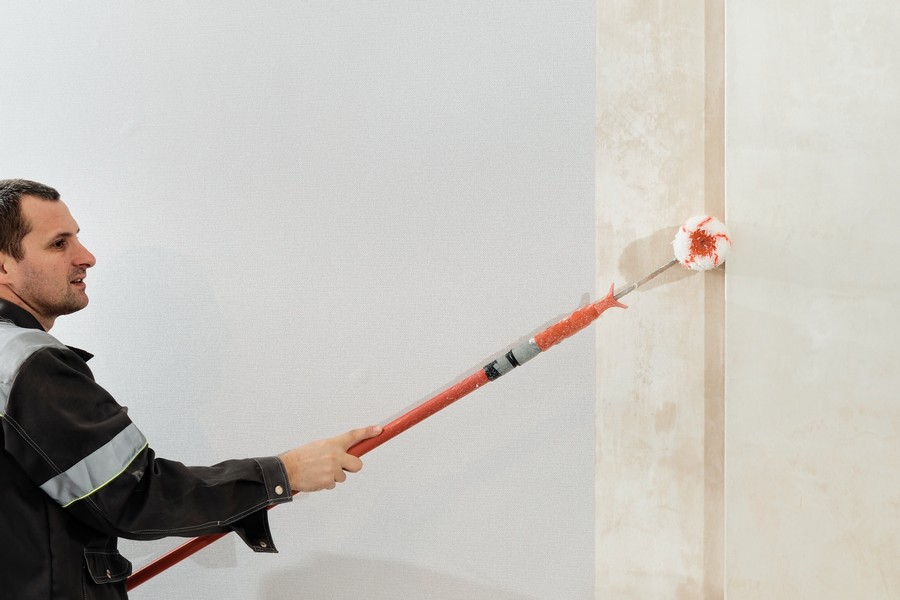 Man worker applies glue with a paint roller on the walls before wallpapering or primer on the walls, selective focus. Apartment renovation and restoration idea indoors.